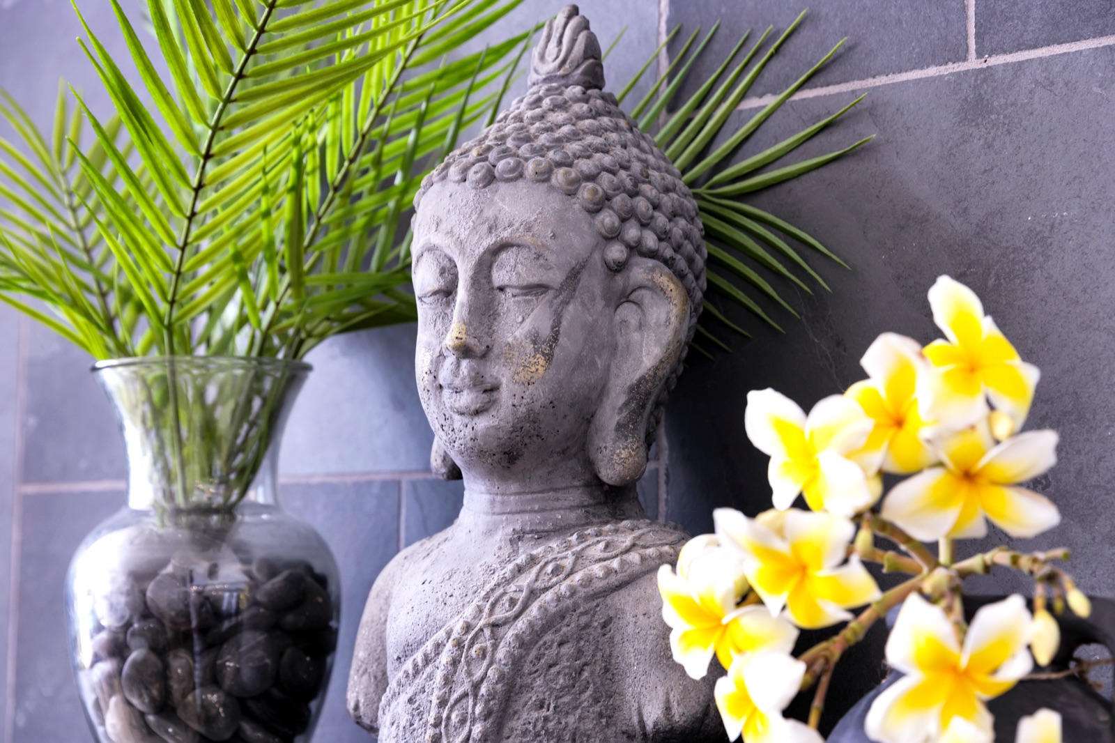 Spa bathroom detail in a luxury Bonaire villa featuring a stone Buddha statue, tropical plumeria flowers, and a natural slate tile wall creating a zen atmosphere.